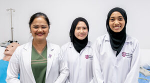 Nursing School in Asia | Female JCHS lecturer and students lab coat black hijab smiling clinical training hospital bed nursing manikin practice